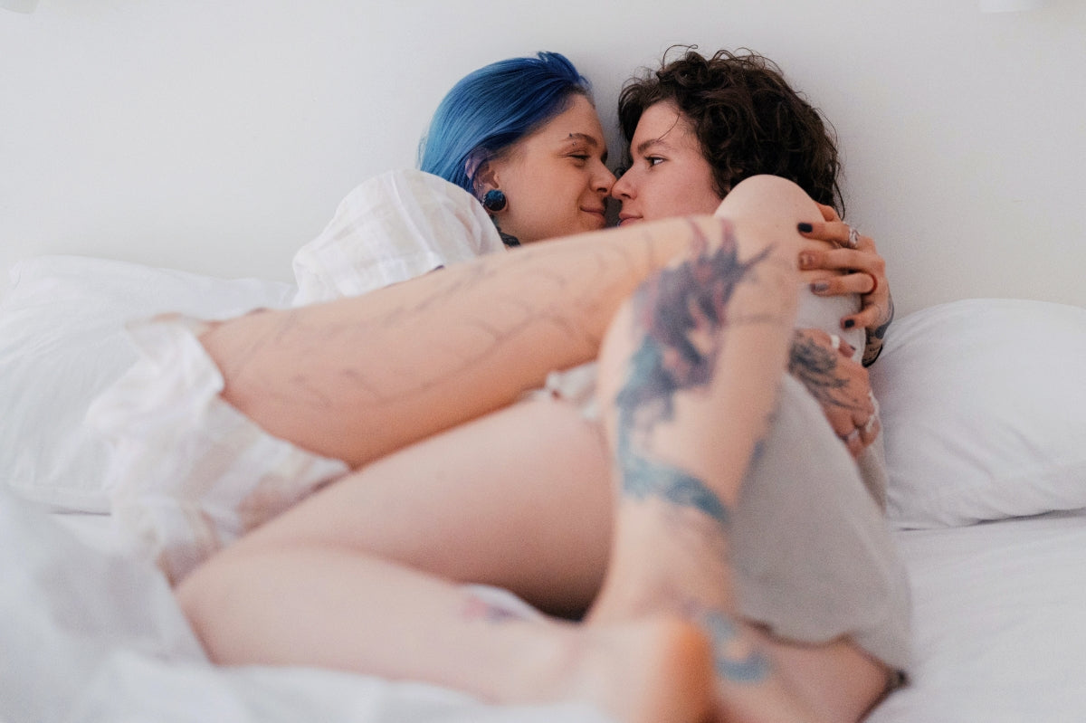 A lesbian couple is intimate in bed with their legs folded over each other